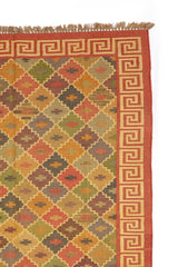 Alfombra kilim tradicional con patrón geométrico en colores cálidos, mostrando detalles de flecos y bordes en tonos rojizos
