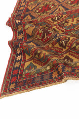 Alfombra kilim con diseño de rombos y figuras geométricas en tonos rojos, dorados y azul marino, con borde de flecos y patrones intrincados.