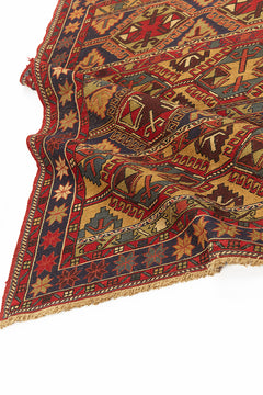 Alfombra kilim con diseño de rombos y figuras geométricas en tonos rojos, dorados y azul marino, con borde de flecos y patrones intrincados.