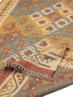 Alfombra rectangular de lana con patrón étnico y flecos. Tonos cálidos y textura natural, ideal para espacios acogedores.