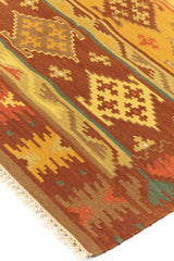 Alfombra kilim con motivos geométricos en tonos marrones, dorados y naranjas, con borde de flecos y detalles intrincados