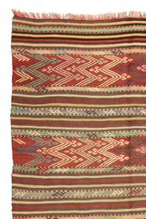 Alfombra kilim con diseño de rayas y patrones geométricos en tonos rojos, verdes y beige, mostrando detalles intrincados y flecos.