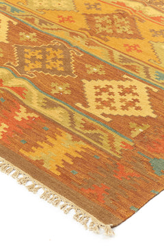 Alfombra kilim con diseño de figuras geométricas en tonos dorados, marrones y naranjas, con borde de flecos decorativos.