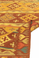 Alfombra kilim con motivos geométricos en tonos marrones, dorados y naranjas, con borde de flecos y detalles intrincados