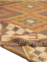 Detalle de una alfombra artesanal de lana con diseño geométrico tribal en tonos tierra y óxido. Motivos naturales y textura rústica.
