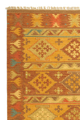 Alfombra kilim con diseño de figuras geométricas en tonos dorados, marrones y naranjas, con borde de flecos decorativos.