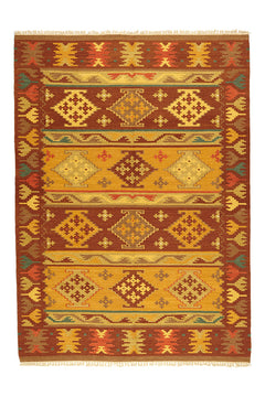 Alfombra kilim con motivos geométricos en tonos marrones, dorados y naranjas, con borde de flecos y detalles intrincados.